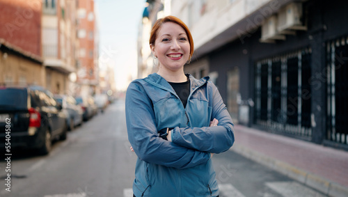 Young redhead woman wearing sportswear standing with arms crossed gesture at street