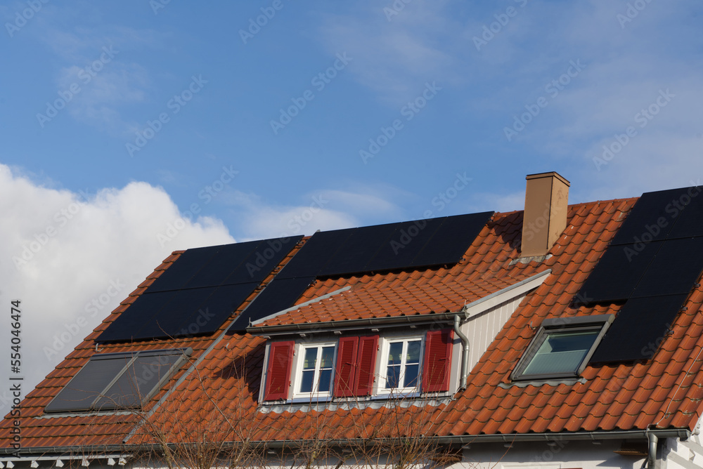 A residential building roof with dormer and skylights. Modern solar modules are laid on the