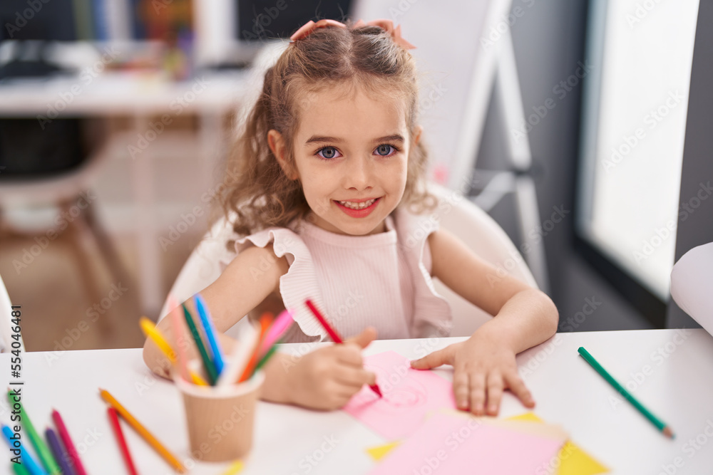 Adorable caucasian girl student sitting on table drawing on paper at classroom Adorable caucasian girl student sitting on table drawing on paper at classroom