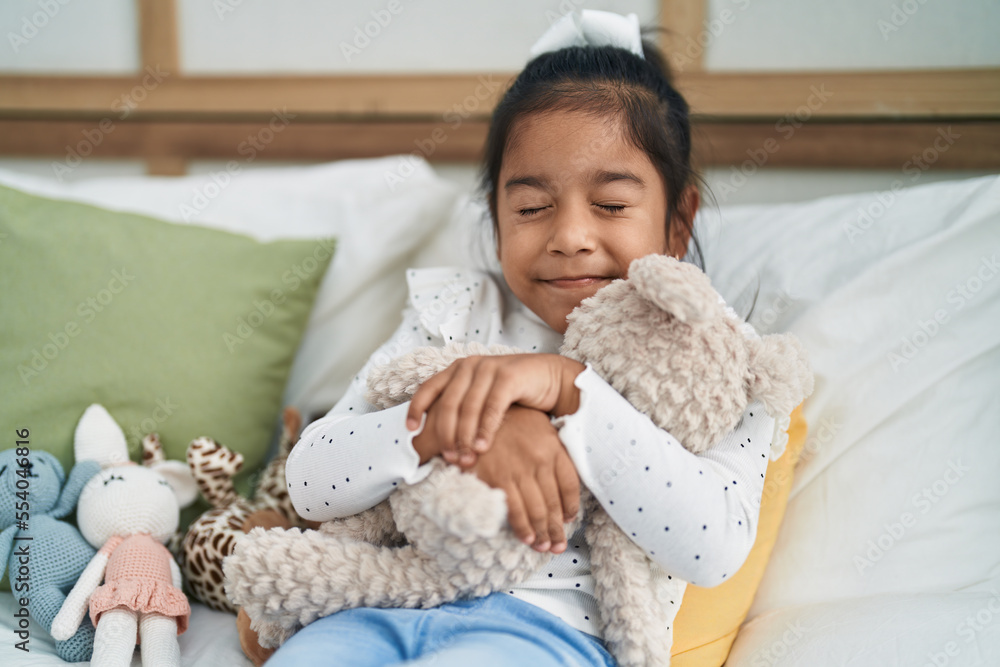 Adorable hispanic girl hugging teddy bear lying on bed at bedroom Adorable hispanic girl hugging teddy bear lying on bed at bedroom