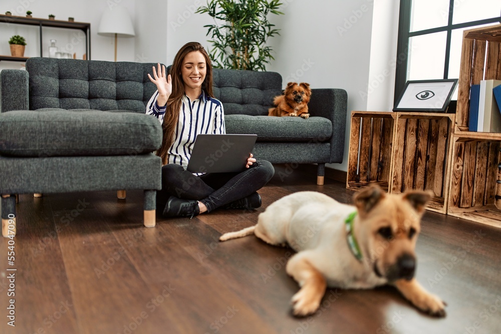 Young hispanic woman having video call sitting on floor with dogs at home