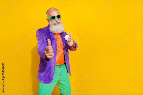 Photo of extravagant senior man two hand direct camera invite you dance wear bright costume empty space isolated on yellow color background