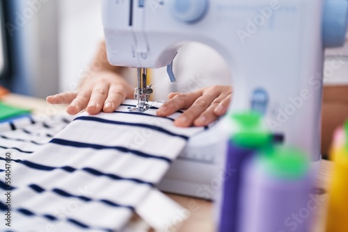 Young beautiful hispanic woman tailor using sewing machine at clothing factory