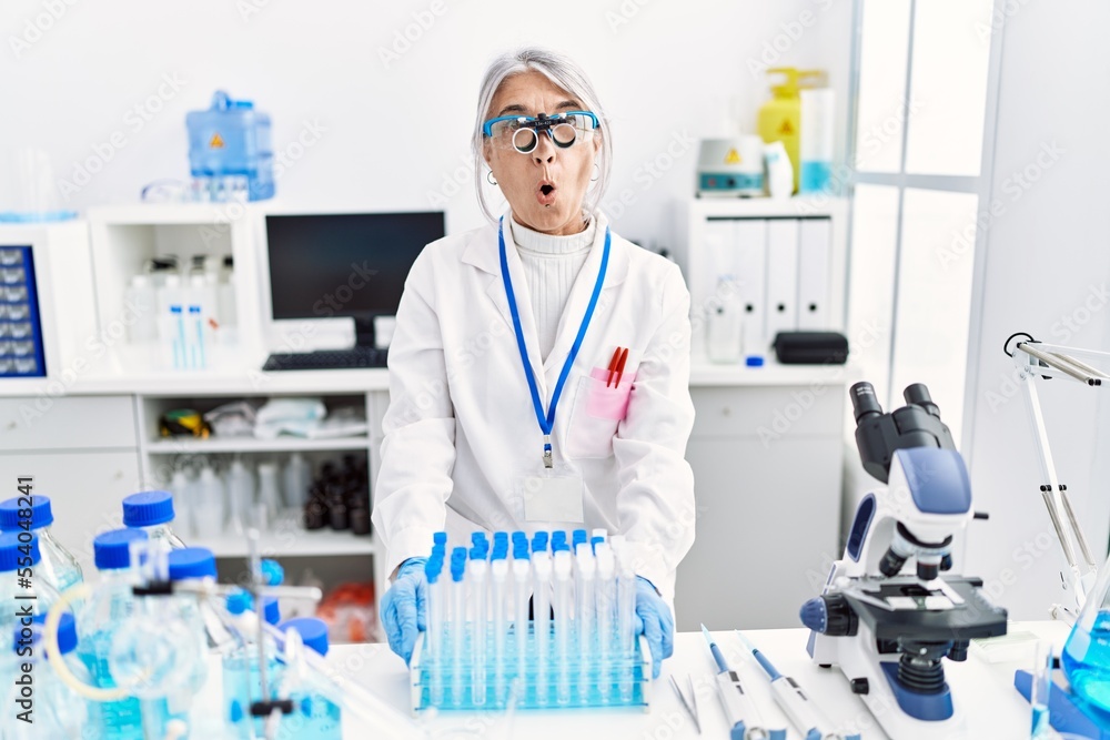 Middle age grey-haired woman wearing scientist uniform scared and amazed with open mouth for surprise, disbelief face Middle age grey-haired woman wearing scientist uniform scared and amazed with open mouth for surprise, disbelief face