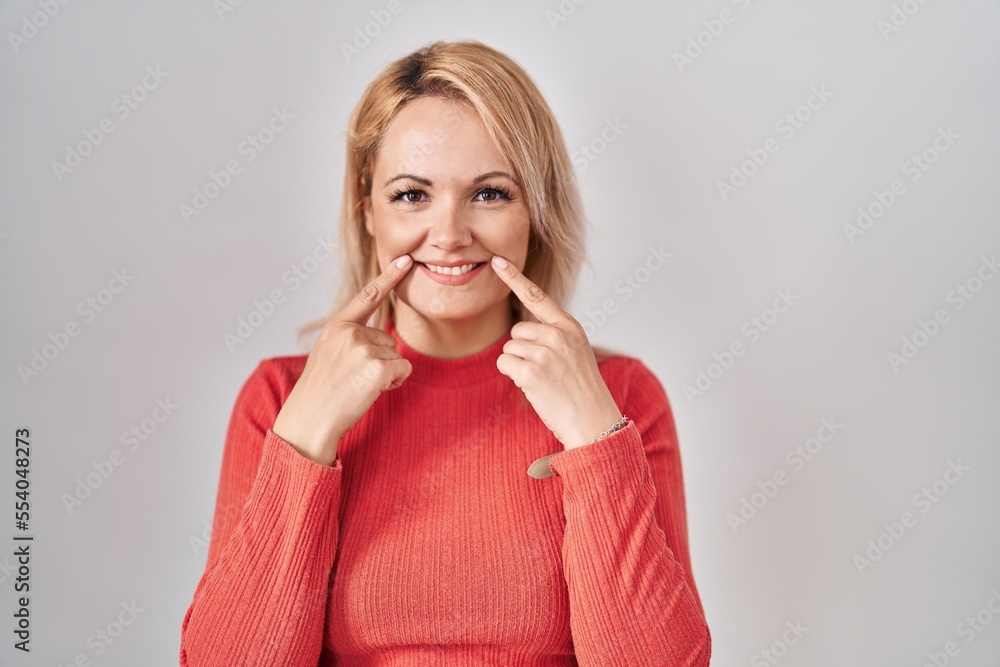 Blonde woman standing over isolated background smiling with open mouth, fingers pointing and forcing cheerful smile Blonde woman standing over isolated background smiling with open mouth, fingers pointing and forcing cheerful smile