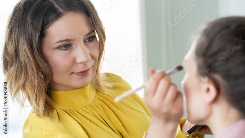 Beauty stylist applying make-up to a young model. Professional Make-up artist doing glamour