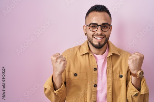 Young hispanic man standing over pink background celebrating surprised and amazed for success with arms raised and open eyes. winner concept. © Krakenimages.com