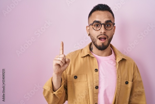 Young hispanic man standing over pink background pointing finger up with successful idea. exited and happy. number one. © Krakenimages.com