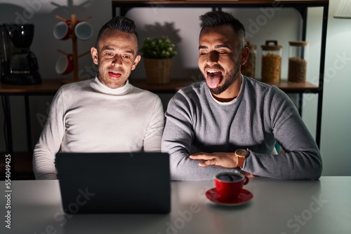 Homosexual couple using computer laptop sticking tongue out happy with funny expression. emotion concept.