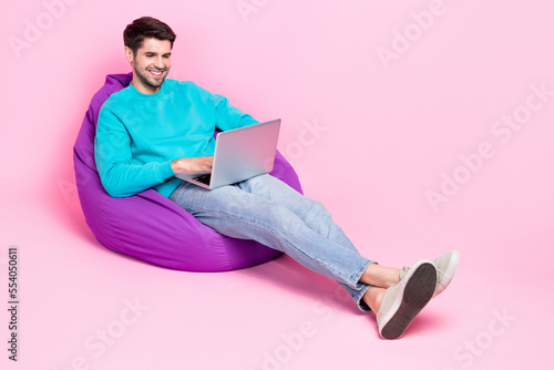 Full size photo of nice young man sitting cozy beanbag netbook online education dressed stylish blue look isolated on pink color background
