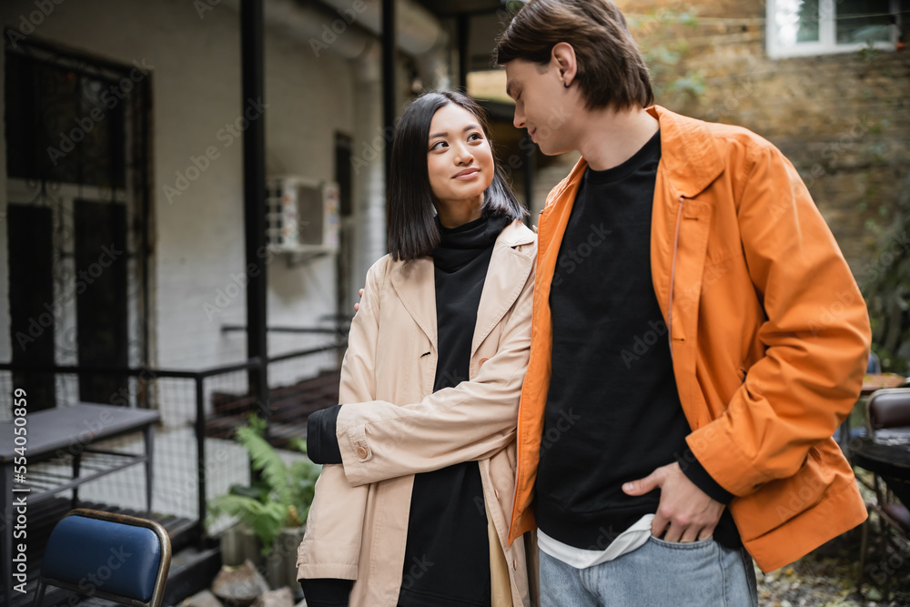 Smiling asian woman looking at stylish boyfriend in outdoor cafe. Smiling asian woman looking at stylish boyfriend in outdoor cafe.