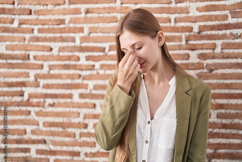 Young caucasian woman standing over bricks wall background tired rubbing nose and eyes feeling fatigue and headache. stress and frustration concept.