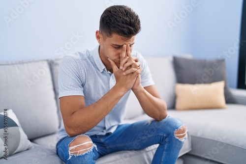 Young hispanic man stressed sitting on sofa at home