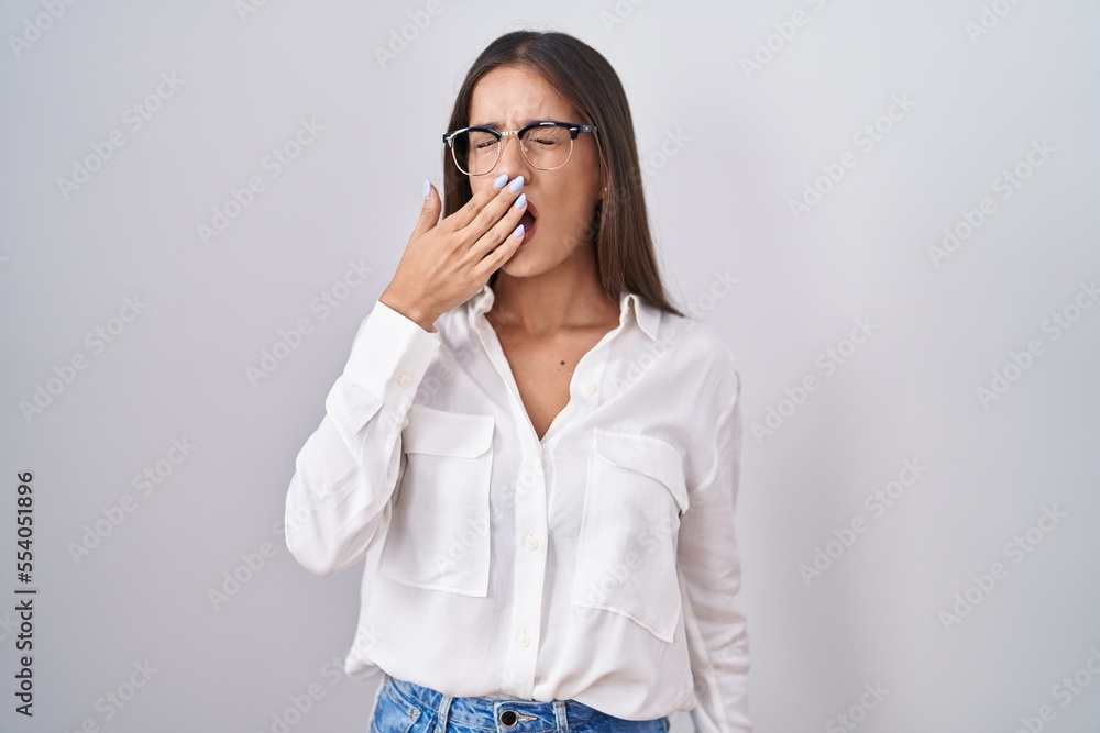 Young brunette woman wearing glasses bored yawning tired covering mouth with hand. restless and sleepiness. Young brunette woman wearing glasses bored yawning tired covering mouth with hand. restless and sleepiness.
