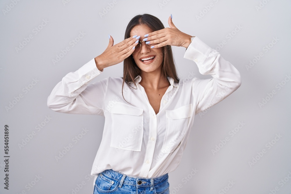 Young brunette woman wearing glasses covering eyes with hands smiling cheerful and funny. blind concept. Young brunette woman wearing glasses covering eyes with hands smiling cheerful and funny. blind concept.