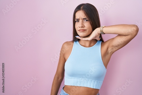 Young brunette woman standing over pink background cutting throat with hand as knife, threaten aggression with furious violence © Krakenimages.com