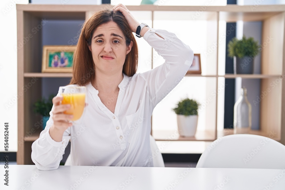 Brunette woman drinking glass of orange juice confuse and wondering about question. uncertain with doubt, thinking with hand on head. pensive concept. Brunette woman drinking glass of orange juice confuse and wondering about question. uncertain with doubt, thinking with hand on head. pensive concept.