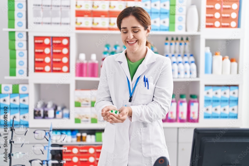 Young woman pharmacist smiling confident holding pills at pharmacy