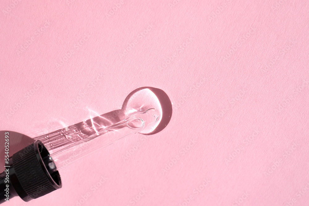 Glass pipette and a round drop of essence on a pink background. flat lay, space for text. Glass pipette and a round drop of essence on a pink background. flat lay, space for text.