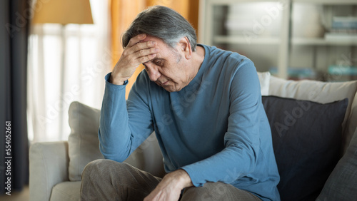 Cuadro en lienzo Old man holding his forehead sitting alone at home