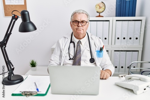 Senior caucasian man wearing doctor uniform and stethoscope at the clinic relaxed with serious expression on face. simple and natural looking at the camera.