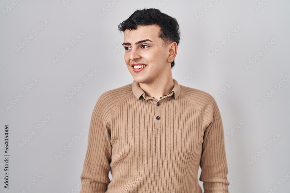 Fototapeta premium Non binary person standing over isolated background looking away to side with smile on face, natural expression. laughing confident.