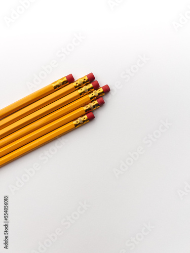 Stationery on office table. Isolated yellow pencils with red rubbered tip on the white background in a row 