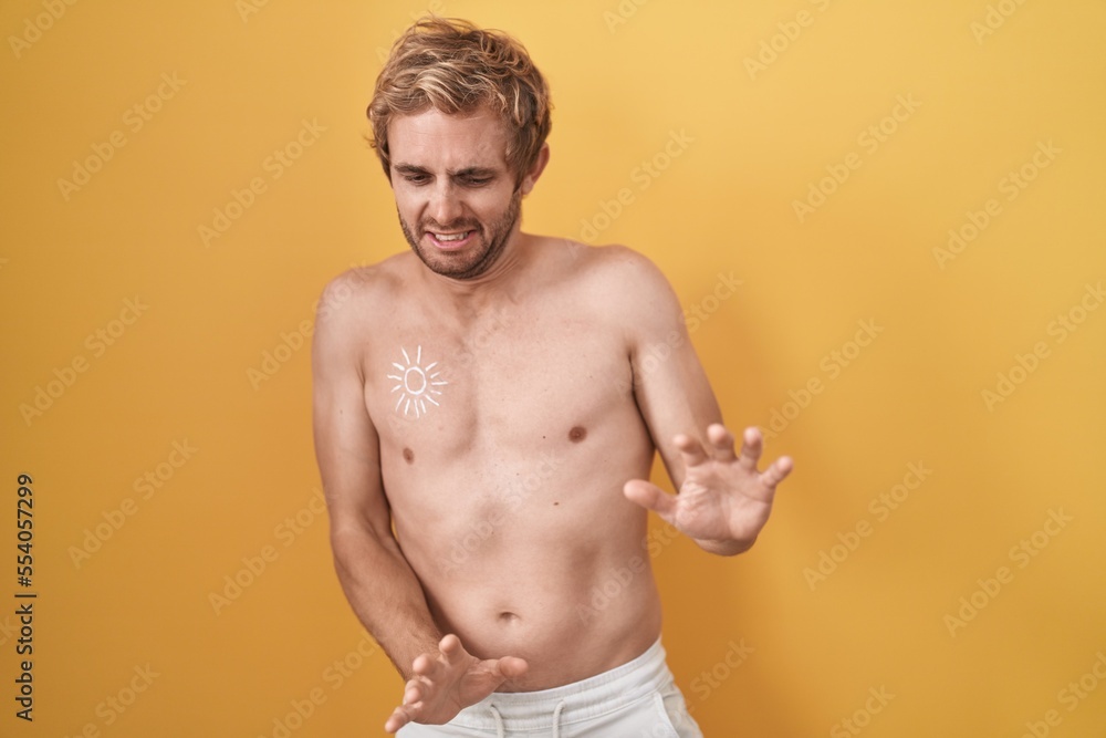 Caucasian man standing shirtless wearing sun screen disgusted expression, displeased and fearful doing disgust face because aversion reaction.
