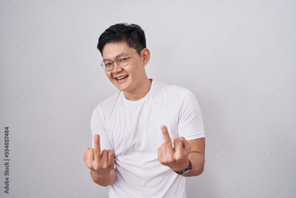 Young asian man standing over white background showing middle finger doing fuck you bad expression, provocation and rude attitude. screaming excited Young asian man standing over white background showing middle finger doing fuck you bad expression, provocation and rude attitude. screaming excited