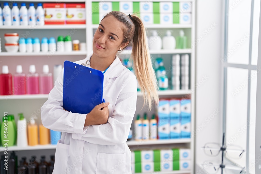 Young beautiful hispanic woman pharmacist smiling confident holding clipboard at pharmacy