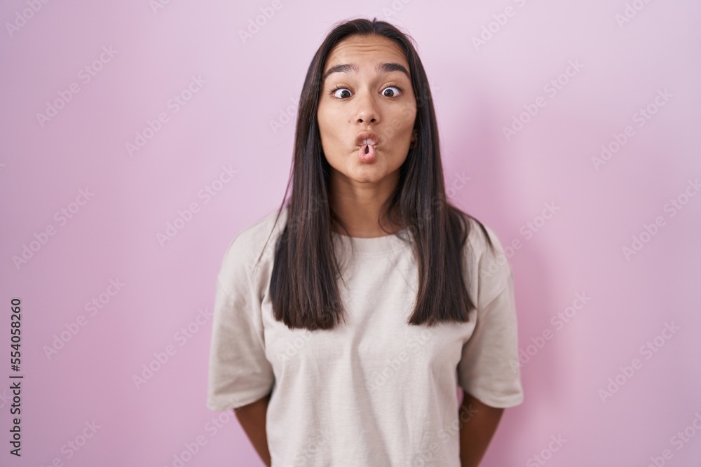 Young hispanic woman standing over pink background making fish face with lips, crazy and comical gesture. funny expression. Young hispanic woman standing over pink background making fish face with lips, crazy and comical gesture. funny expression.