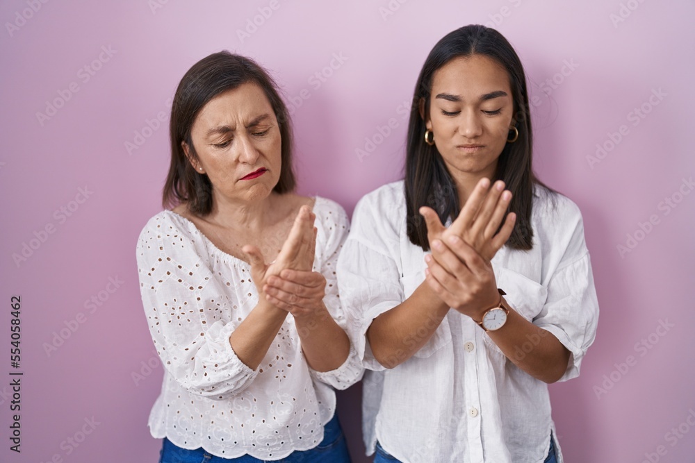 Hispanic mother and daughter together suffering pain on hands and fingers, arthritis inflammation Hispanic mother and daughter together suffering pain on hands and fingers, arthritis inflammation