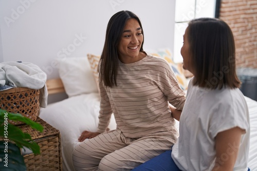 Two women mother and daughter hugging each other sitting on bed at bedroom