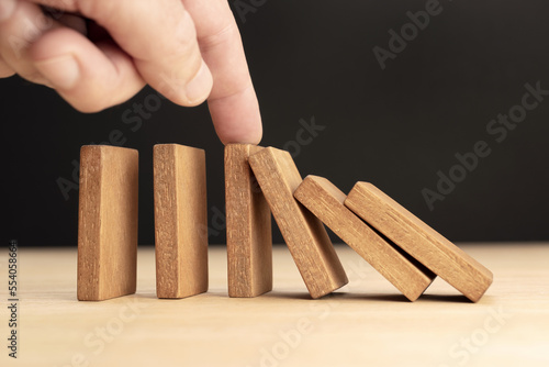 Hand Stopping Falling wooden Dominoes effect