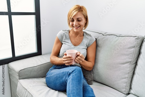 Middle age blonde woman smiling confident drinking coffee at home