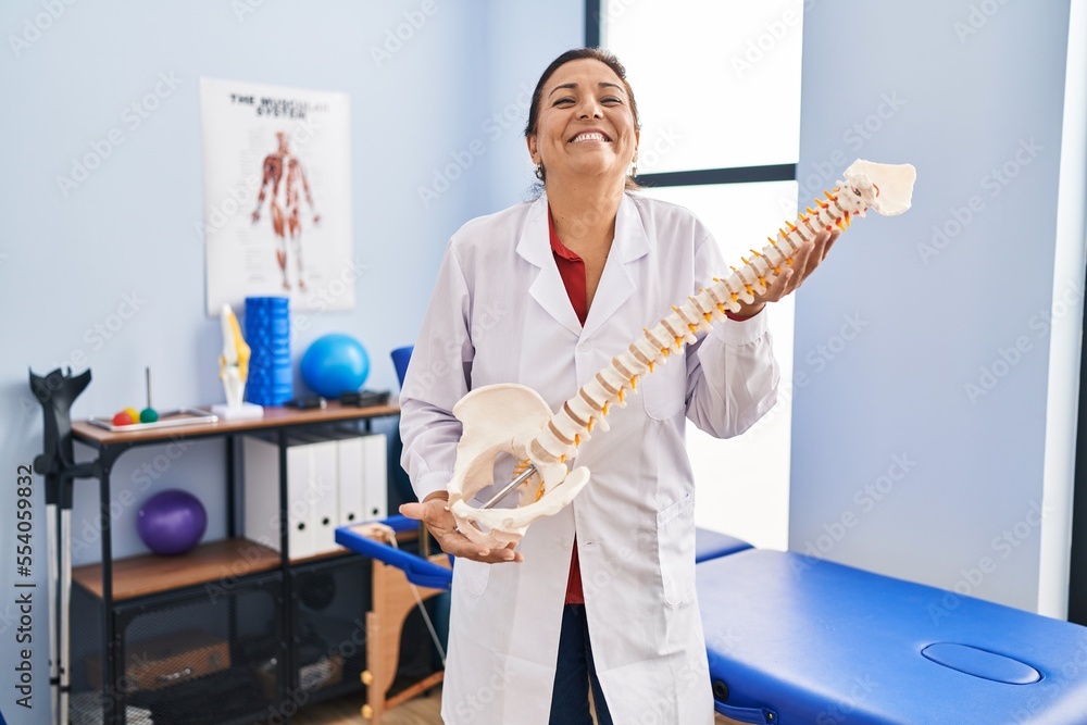 Φωτογραφία Middle age hispanic woman holding anatomical model of spinal column smiling and laughing hard out loud because funny crazy joke