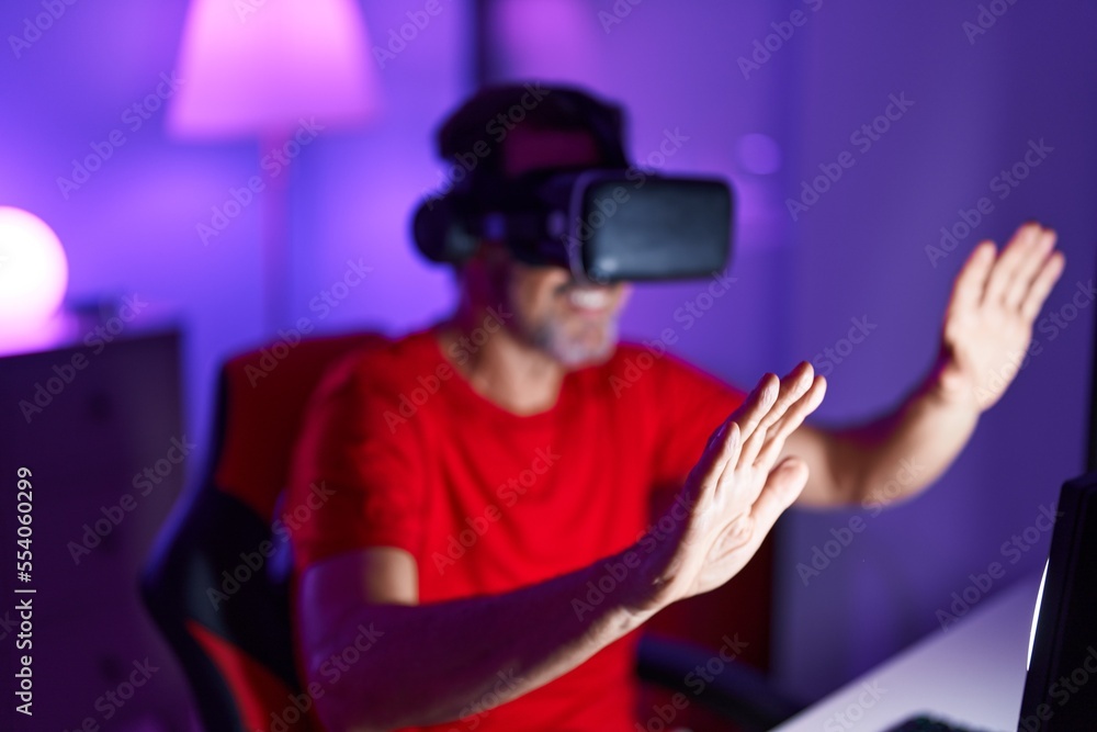 Middle age man streamer playing video game using virtual reality glasses at gaming room Middle age man streamer playing video game using virtual reality glasses at gaming room