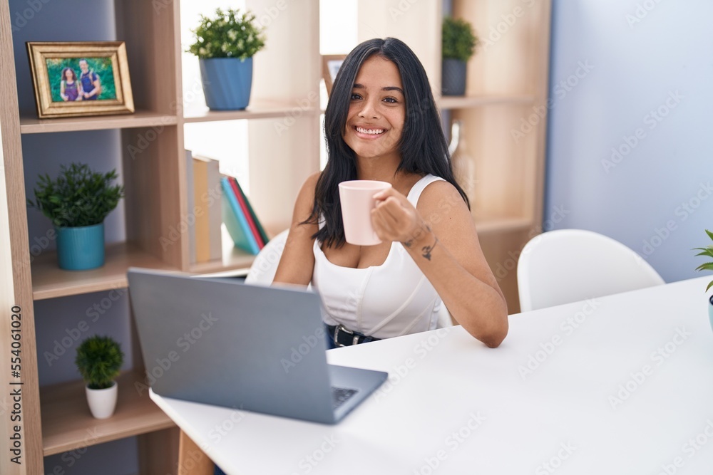 Young hispanic woman using laptop drinking coffee at home Young hispanic woman using laptop drinking coffee at home