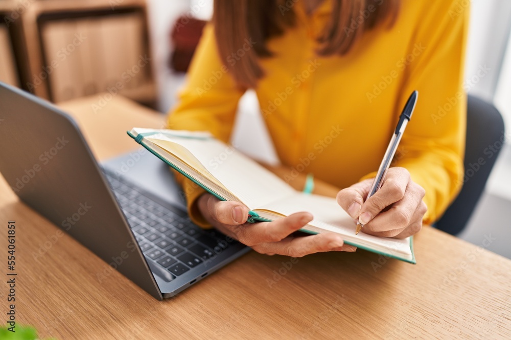 Young woman business worker writing on book using laptop working at office Young woman business worker writing on book using laptop working at office