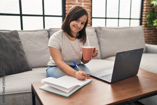 Down syndrome woman smiling confident working sitting on sofa at home