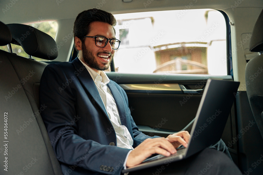 Attractive businessman in suit working laptop while riding in car to office