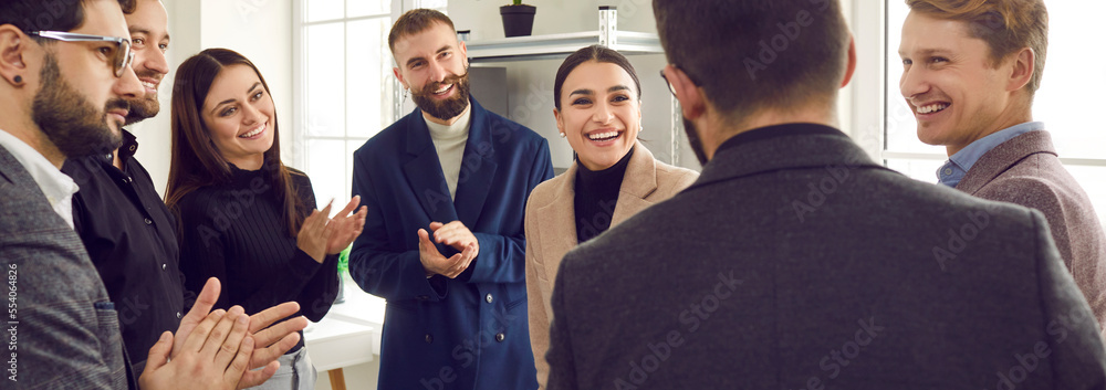 Obraz premium Happy business team congratulating their colleague on job promotion and professional success. Group of happy people looking at young man, applauding and smiling. Banner. Recognition at work concept