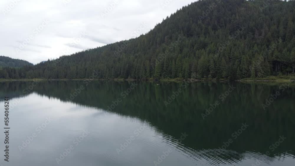 Boom up camera movement over the calm lake surrounded by green forest Boom up camera movement over the calm lake surrounded by green forest