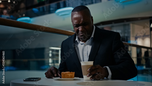 African American middle-aged businessman entrepreneur cafe visitor man sitting eating in cafeteria dissatisfied with bad cake disgust pie dessert trouble drink nasty tea tasteless coffee unpleasant photo