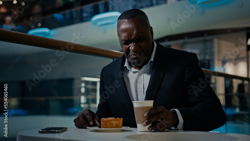 African American middle-aged businessman entrepreneur cafe visitor man sitting eating in cafeteria dissatisfied with bad cake disgust pie dessert trouble drink nasty tea tasteless coffee unpleasant