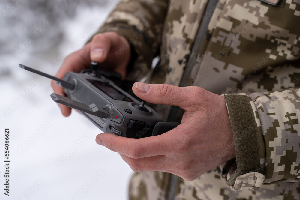 military operator in winter camouflage uniform controls the quadcopter, holding the remote control in his hands. using a drone for reconnaissance and surveillance of enemy troops in a secial forces,