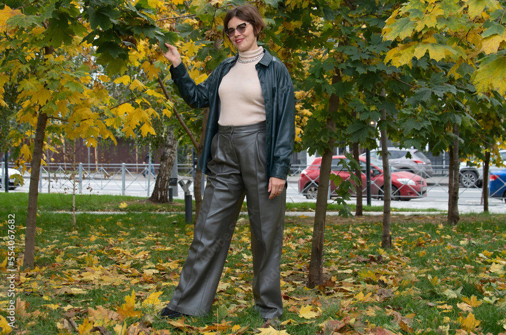 A woman in leather clothes stands against the backdrop of an autumn maple square