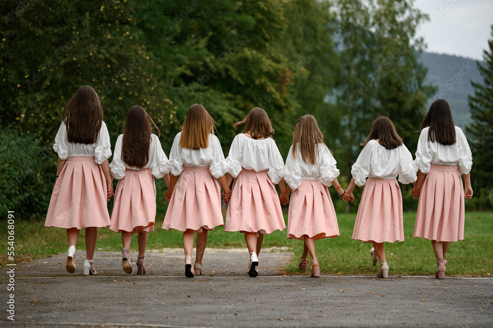 The girls walk forward on the grass in identical blouses and skirts.