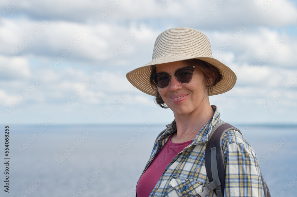 Portrait of a tourist woman in a straw hat standing on the shore on a sunny summer day