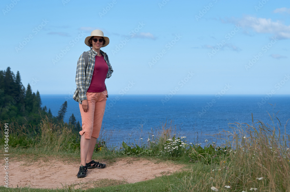 Portrait of a tourist woman in a straw hat standing on the shore on a sunny summer day